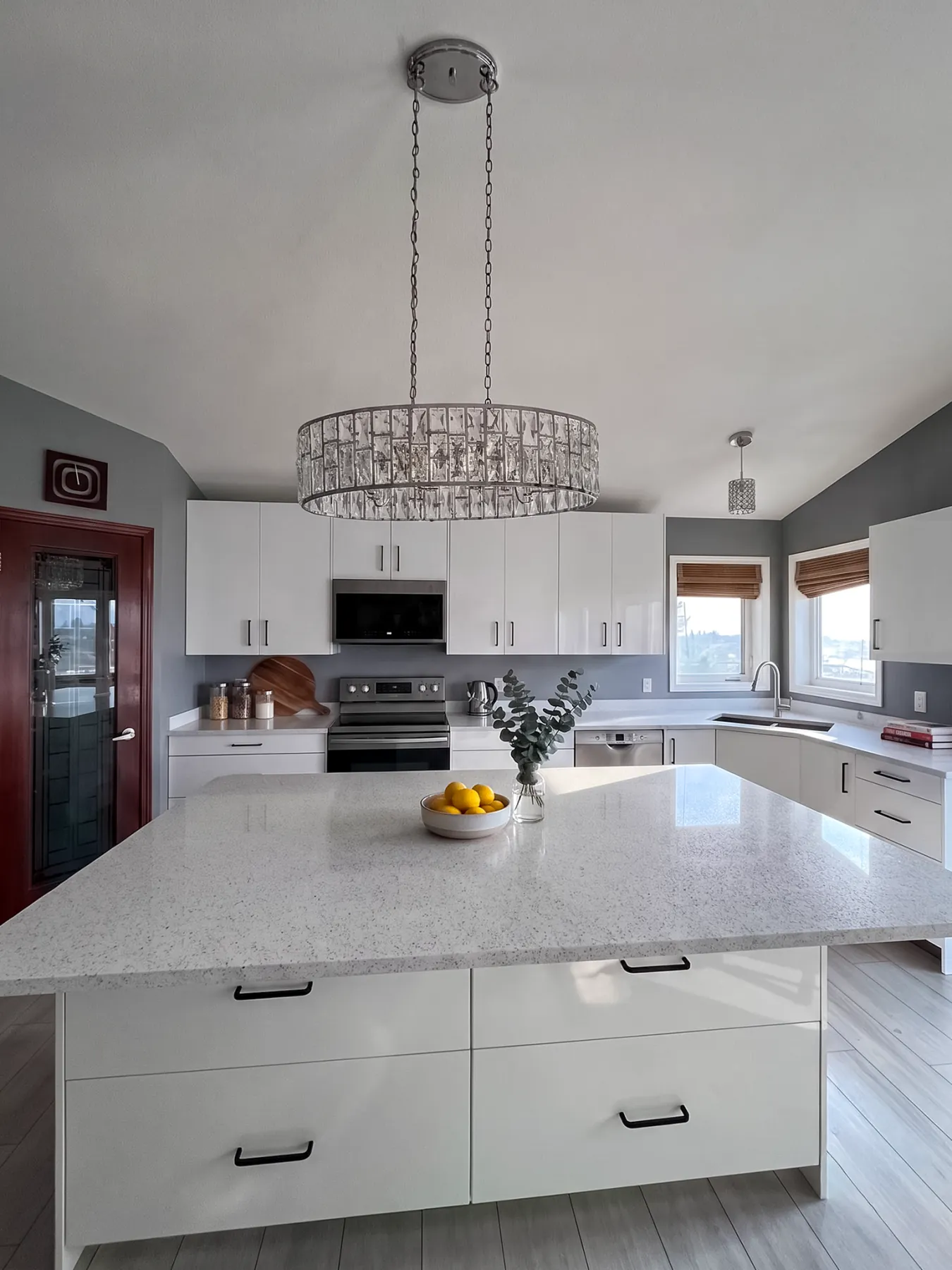 Square seating island in speckled white quartz under a crystal drum chandelier